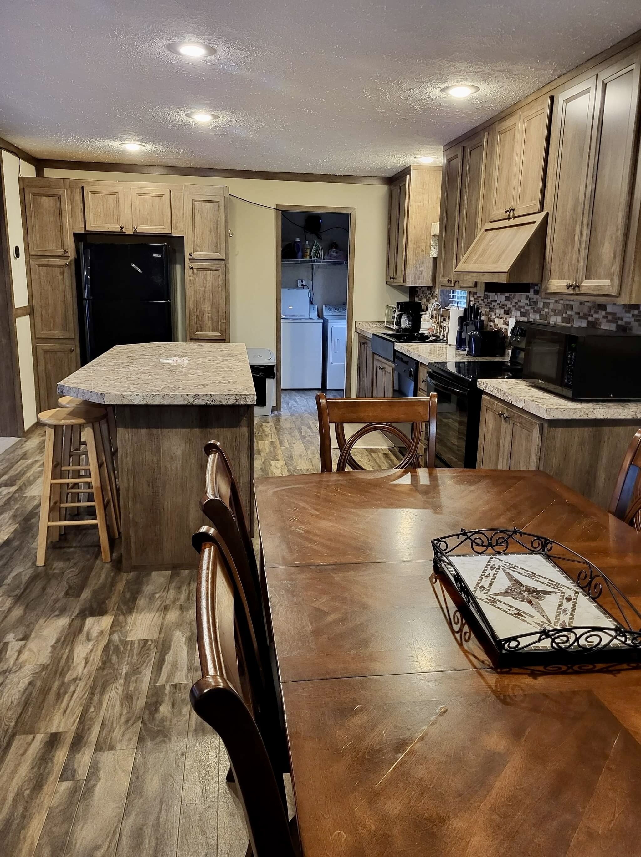 A kitchen with wooden cabinets, a black refrigerator, a stove, and a microwave. There is a dining table with chairs and a small ladder.