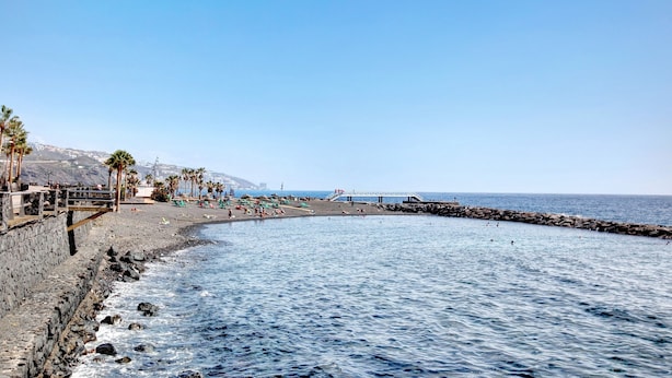 A coastal beach with a stone wall, palm trees, and a clear blue sky. - Holiday Home "Casa Roberto" with Private Balcony, Shared Pool and Wi-Fi (Candelaria)