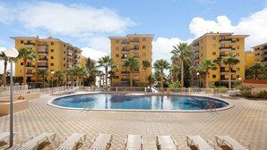 A pool area with lounge chairs, a pool, and multi-story yellow buildings with balconies. - Holiday Home "Casa Roberto" with Private Balcony, Shared Pool and Wi-Fi (Candelaria)