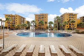 A pool area with lounge chairs, a pool, and multi-story yellow buildings with balconies.