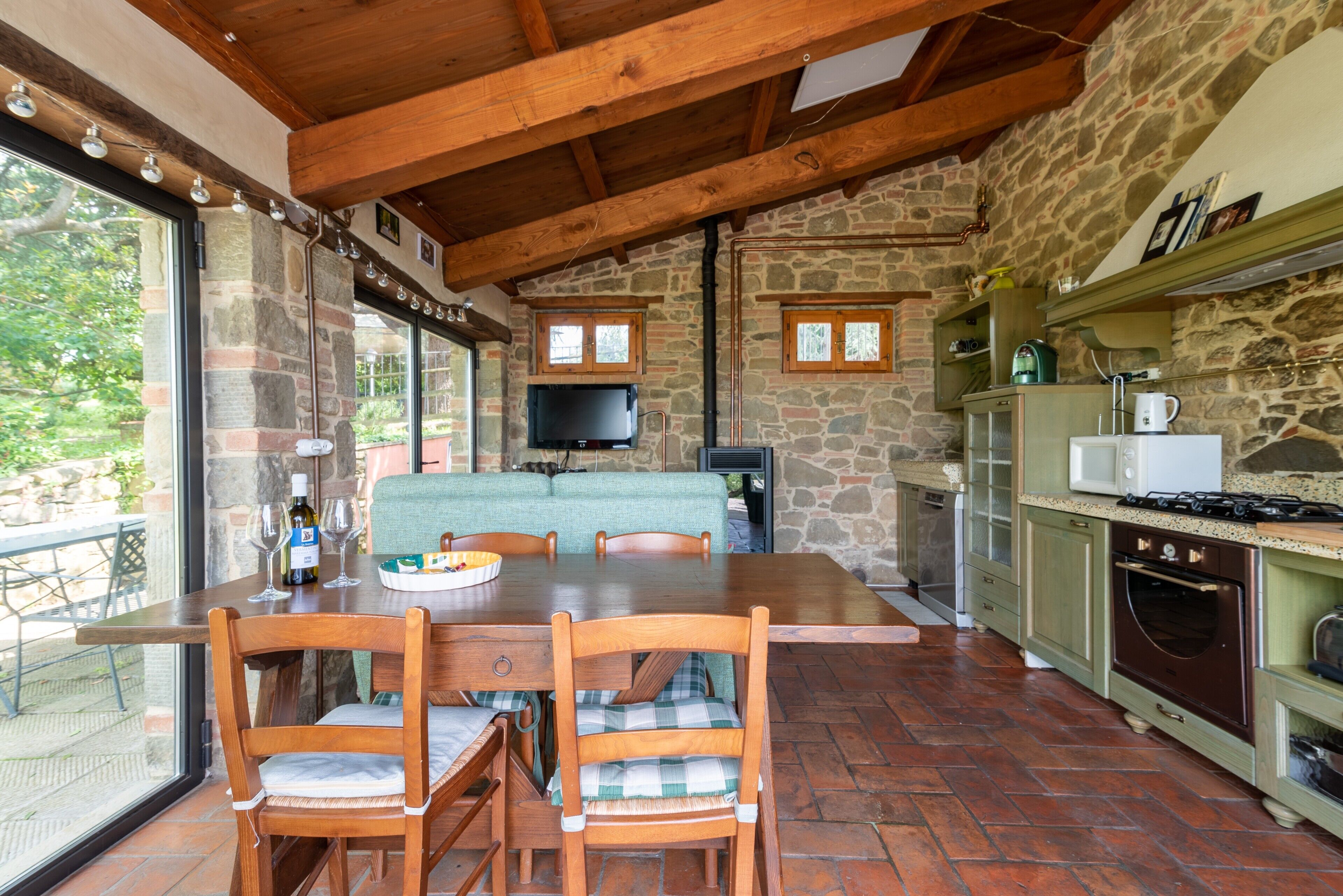 Une cuisine aux murs de pierre, avec une table et des chaises en bois, un téléviseur et une cheminée en pierre.