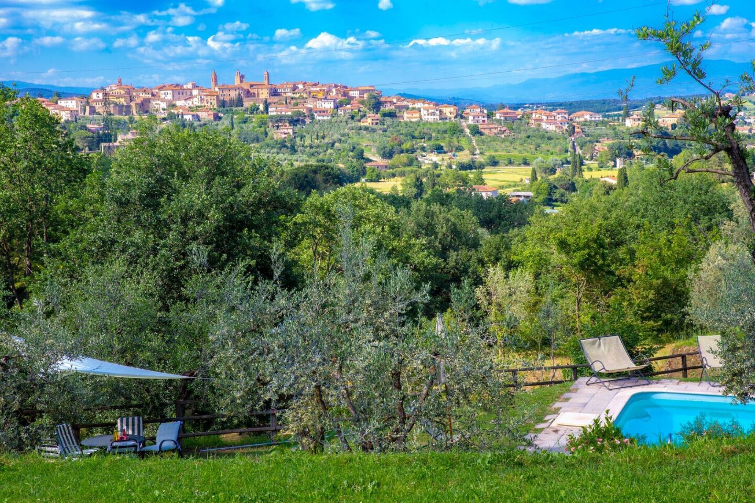 Ein Poolbereich mit Liegestühlen, einer Pergola und Blick auf eine Stadt mit historischen Gebäuden.