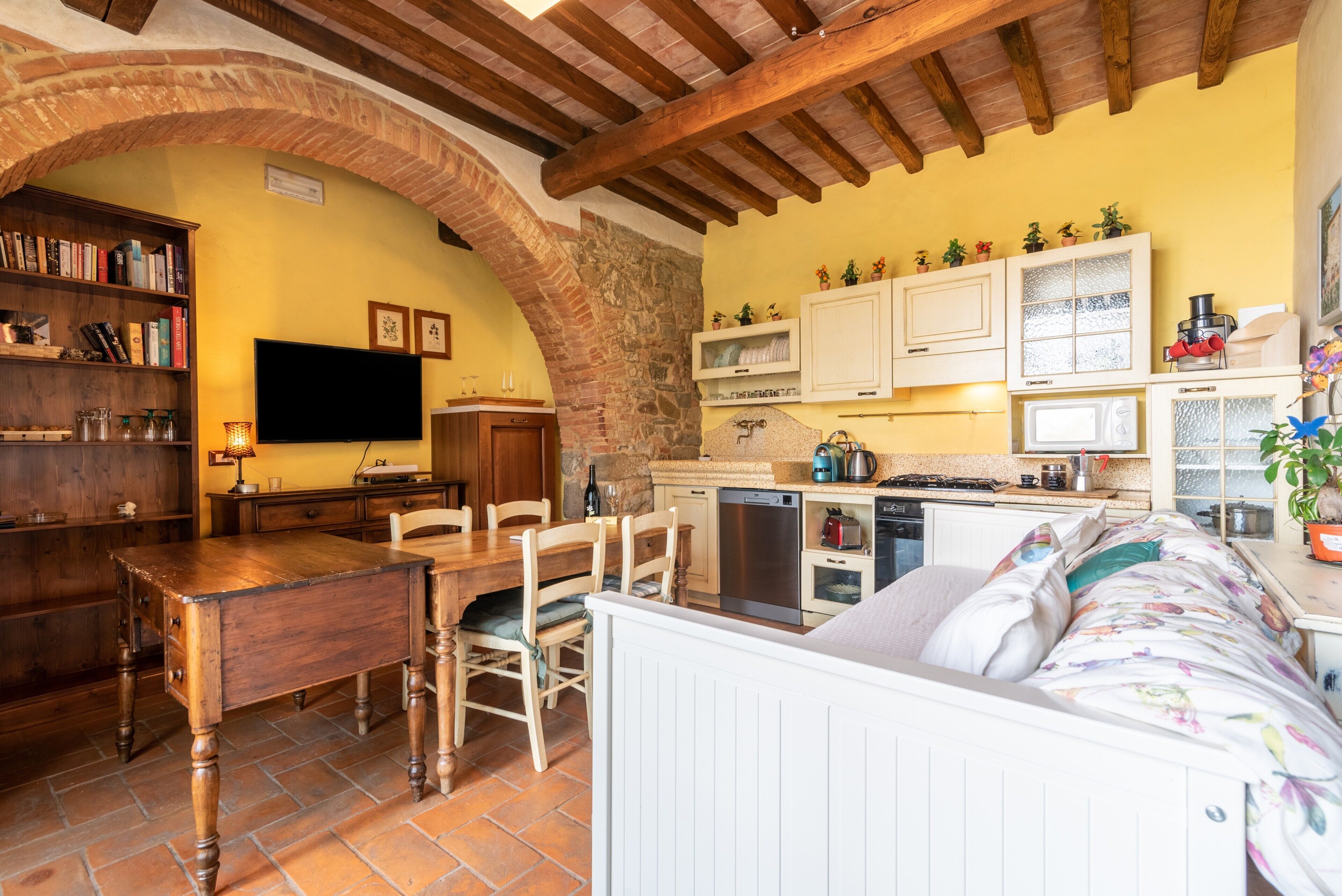Une cuisine chaleureuse avec un coin repas, un téléviseur fixé au mur et une arche en pierre.