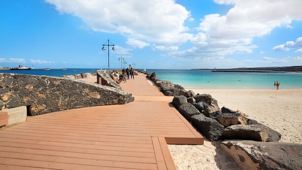 A wooden boardwalk leading to a beach with a stone wall on one side and a rocky shoreline on the other.