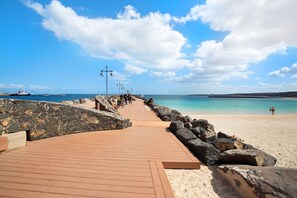 Un muelle de madera que conduce a una playa, con un muro de piedra a un lado y una costa rocosa al otro.