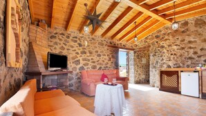 A rustic interior with a stone wall, wooden beams, a sofa, a table with a white tablecloth, and a television.