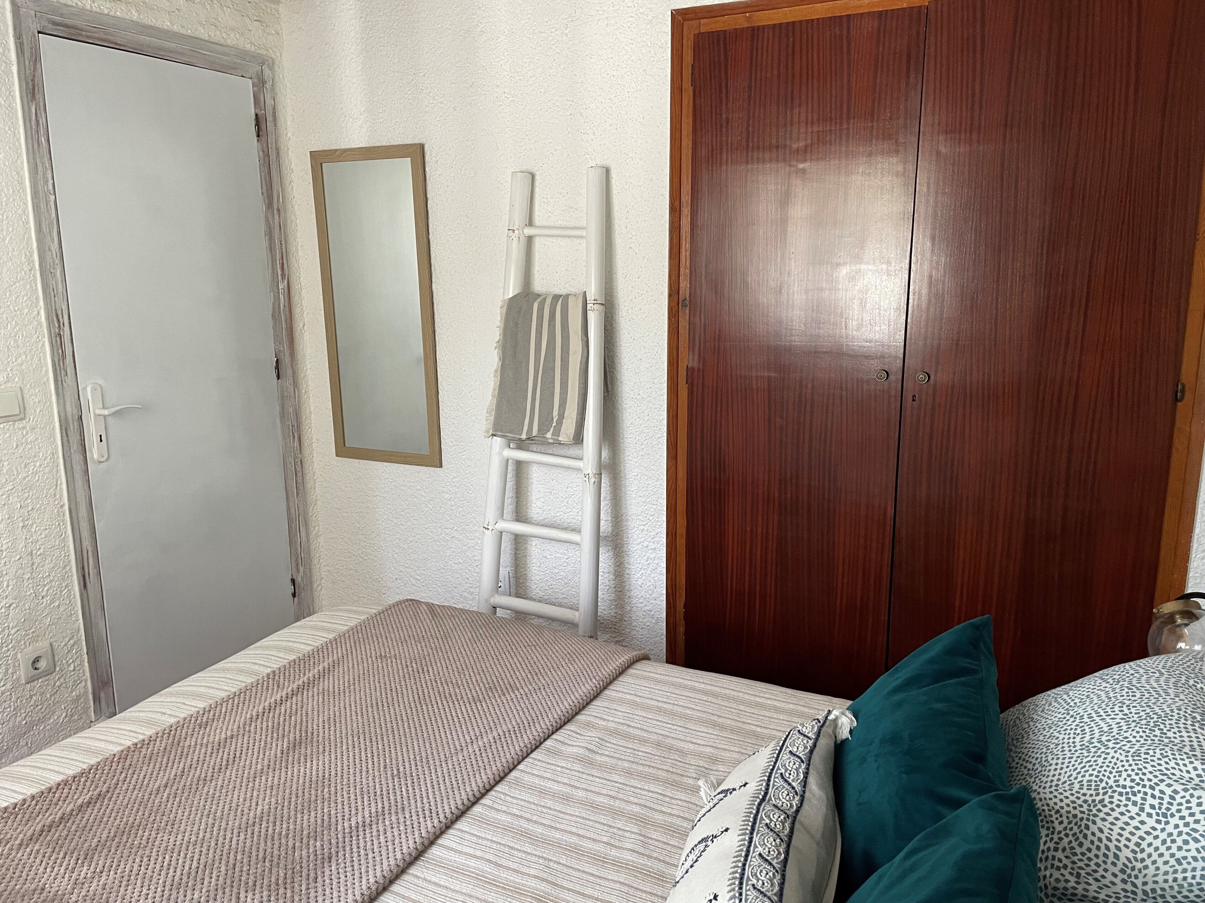 Ein Schlafzimmer mit einem Bett, einem Holzschrank, einer weißen Tür und einem Spiegel.