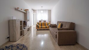 A living room with a sofa, a TV stand, and a patterned ottoman. - Holiday Home "Casa Kennedy" near the Beach with Balcony & Wi-Fi (monopoli)