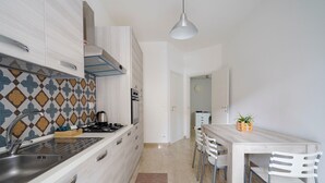 A modern kitchen with white cabinets, a patterned backsplash, and a dining area with a wooden table and chairs. - Holiday Home "Casa Kennedy" near the Beach with Balcony & Wi-Fi (monopoli)