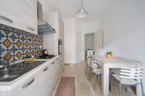 Una cocina moderna con armarios blancos, un salpicadero con diseño y un comedor con mesa y sillas de madera.