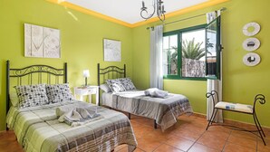 Una stanza con due letti, una panca, un lampadario e una finestra vista palme.