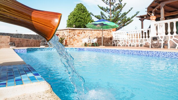 Una piscina con acqua cristallina, un muro in pietra e un pergolato in legno.