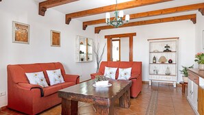 Un soggiorno con soffitto in legno, divani rossi, un tavolino da caffè in legno e un mobiletto bianco con scaffali.