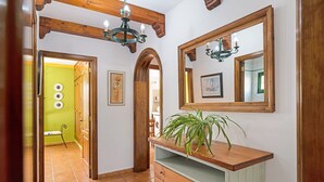 Un corridoio con travi in legno, un lampadario, uno specchio e una pianta su una consolle di legno.