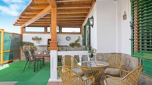 Un'area patio coperta con mobili in vimini, un muro in pietra e una recinzione verde.