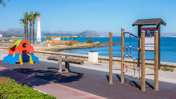 Uma passarela costeira com um parquinho, um farol e uma estrutura de madeira com painéis informativos.