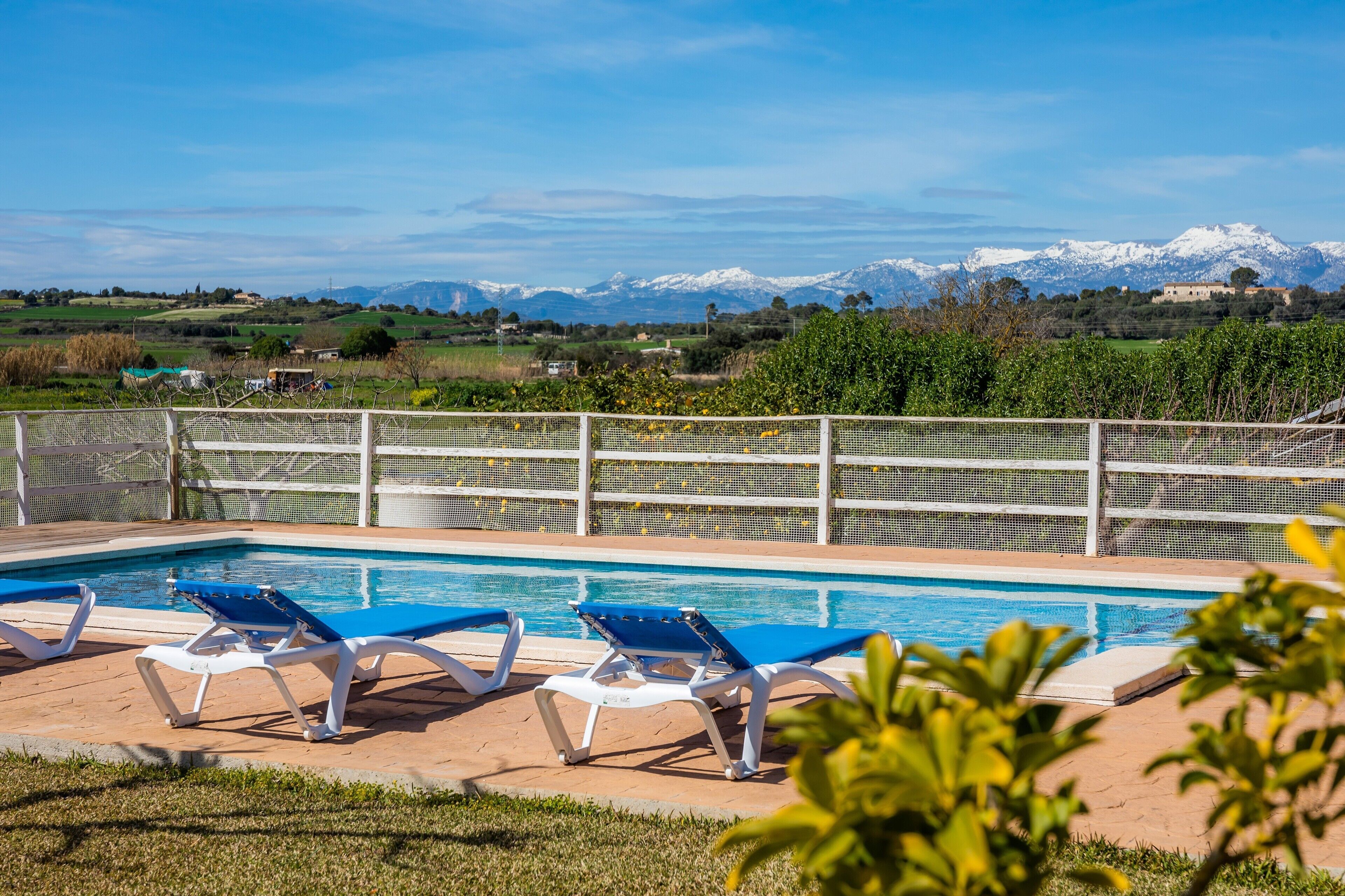 A pool with blue chairs, a white fence, and a mountain view.