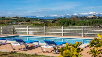 A pool with blue chairs, a white fence, and a mountain view.