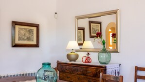 A dining area with a wooden table, chairs, a vase with flowers, a lamp, a mirror, and framed pictures on the wall. - Casa "Cova Dor" with Shared Pool, Garden and Wi-Fi (Santa Margalida)