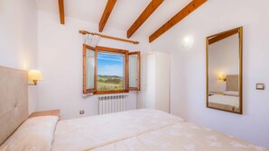 A bedroom with a bed, a window with a view, a mirror, and a radiator. - Casa "Cova Dor" with Shared Pool, Garden and Wi-Fi (Santa Margalida)