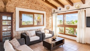 A room with stone walls, wicker furniture, a wooden ceiling, and large windows with curtains. - Finca "Can Jeroni" with Private Terraces, Private Pool & Wi-Fi (Felanitx)