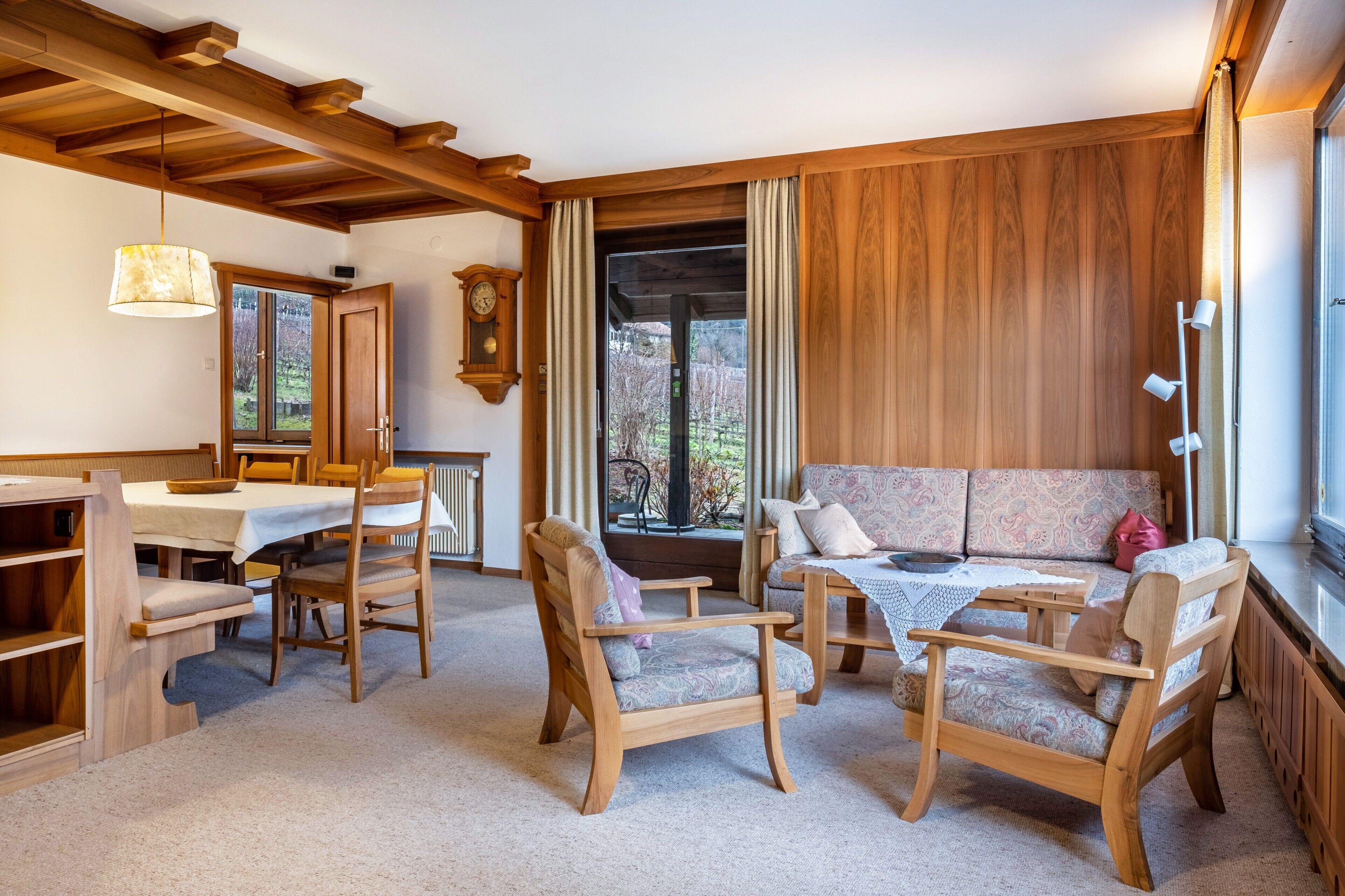 A cozy room with wooden furniture, a dining table, a sofa, and a view through a window.