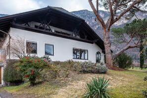Un edificio blanco con techo oscuro, rodeado de árboles y un paisaje montañoso.