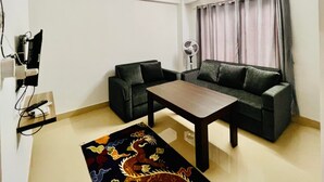 Ein kleiner, helles Wohnzimmer mit einer Couch, einem Couchtisch und einem Ventilator.