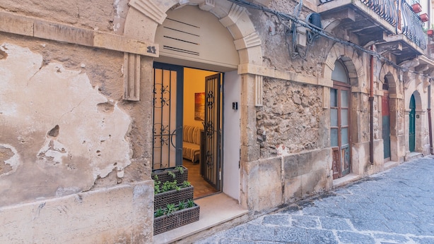 A historic building with a stone facade, a wooden door, and a small outdoor seating area with plants. - Apartment 'Casa Pepes Centro Ortigia' with Shared Garden, Wi-Fi and Air Conditioning (Siracusa)