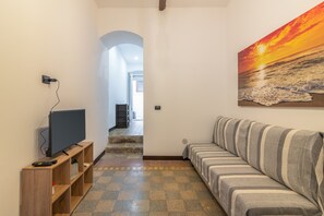 A living room with a sofa, a television on a stand, and a painting of a sunset.