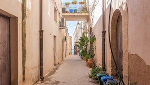 A narrow alley with potted plants and a wooden door on the left. - Apartment 'Casa Pepes Centro Ortigia' with Shared Garden, Wi-Fi and Air Conditioning (Siracusa)