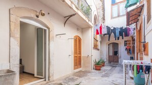 A narrow alleyway with a door, a wooden shutter, and a balcony with clothes hanging. - Apartment 'Casa Pepes Centro Ortigia' with Shared Garden, Wi-Fi and Air Conditioning (Siracusa)