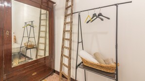 A room with a wooden wardrobe, a ladder, a metal rack with hangers, and a wicker basket. - Apartment 'Casa Pepes Centro Ortigia' with Shared Garden, Wi-Fi and Air Conditioning (Siracusa)