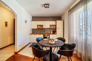 Une cuisine moderne avec un coin repas, comprenant une table ronde entourée de chaises, un panier de fruits et une horloge murale.