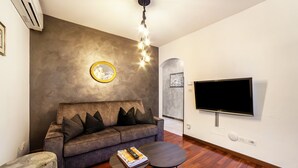A modern living room with a sofa, a coffee table, a TV mounted on the wall, and a unique light fixture. - Holiday Apartment 'König - The King 4th' with Balcony & Wi-Fi (Meran)