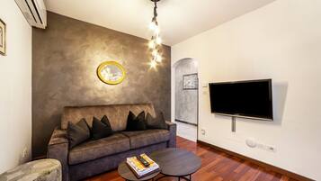 Ein modernes Wohnzimmer mit einer Couch, einem Couchtisch, einem an der Wand befestigten Fernseher und einer besonderen Leuchte.