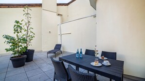 A patio with a table, chairs, potted plants, and a bottle of water.