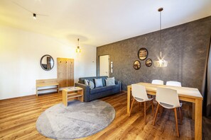 A modern living room with a sofa, dining table, chairs, a round rug, and a wooden bench.