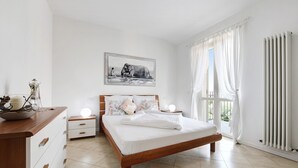 A bedroom with a wooden bed, white walls, a painting of an elephant, a nightstand with a lamp, and a radiator.