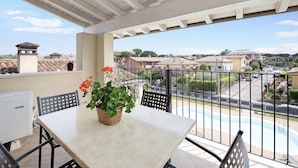 A balcony with a table and chairs, a potted plant, and a view of a residential area.