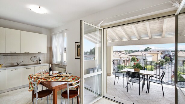 A kitchen with a dining area, a glass door leading to a balcony with outdoor furniture.