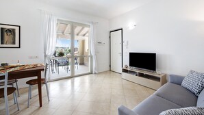 A modern living room with a sofa, a TV, a dining table with chairs, and a sliding glass door leading to an outdoor area.