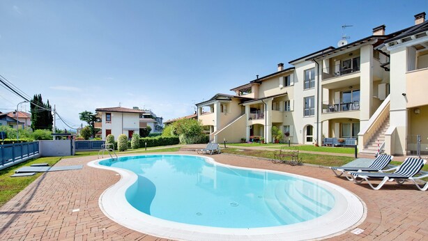 Una piscina con lettini, un patio in mattoni e edifici a più piani sullo sfondo.