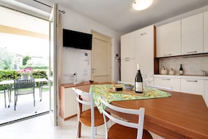 A modern kitchen with white cabinets, a wooden dining table, and a TV mounted above the door.
