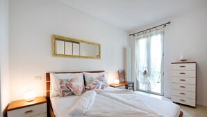 Un letto rifatto con cuscini, una lampada da comodino, una cassettiera e una finestra con tende.