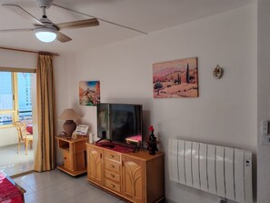 A living room with a ceiling fan, a TV, a radiator, and artwork on the walls.