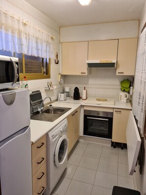 A compact kitchen with a washing machine, a microwave, a toaster, and a sink.