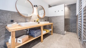 Ein modernes Badezimmer mit zwei Waschbecken, einem Holzlager für die Kosmetik, Marmorfliesen und einem Handtuchhalter.