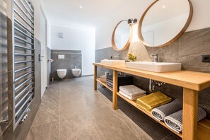 A modern bathroom with a wooden vanity, two sinks, a large mirror, and a towel rack.