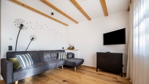 A modern living room with a grey sectional sofa, wooden flooring, a dark dresser, a mounted TV, and a wall art piece. - Holiday Apartment "Binderhof Apt Obm" with Mountain View, Private Terrace and Wi-Fi (Brixen)
